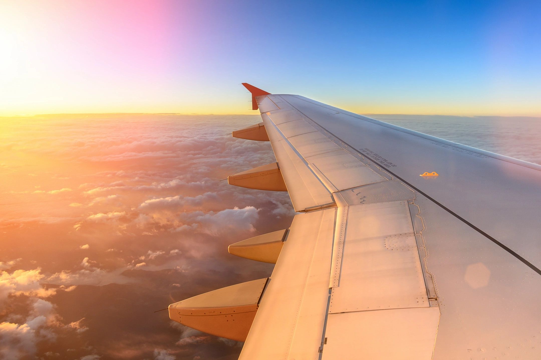 View of an airplane wing over clouds during sunrise.
