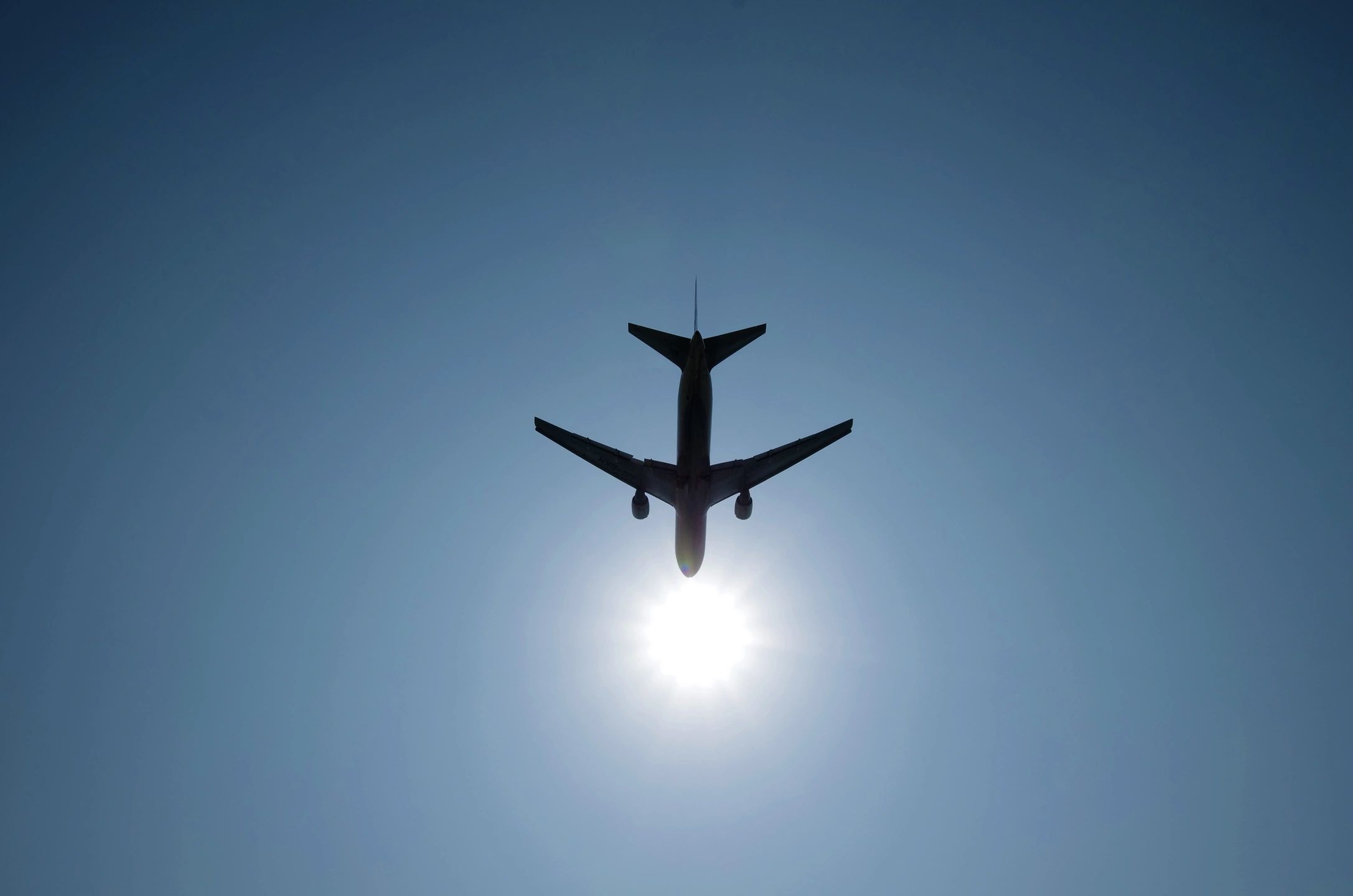 Silhouette of an airplane flying directly above the sun in a clear blue sky.