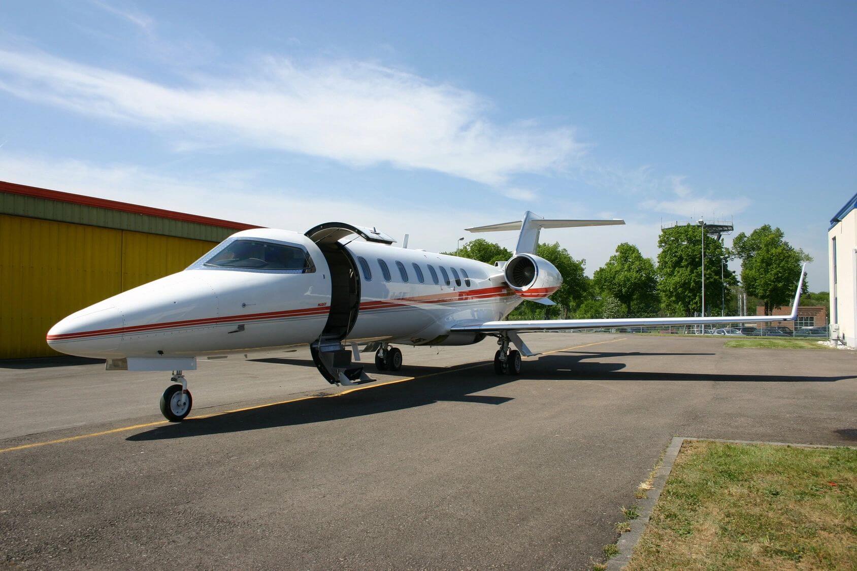 Private jet parked on a runway with door open under a clear sky.